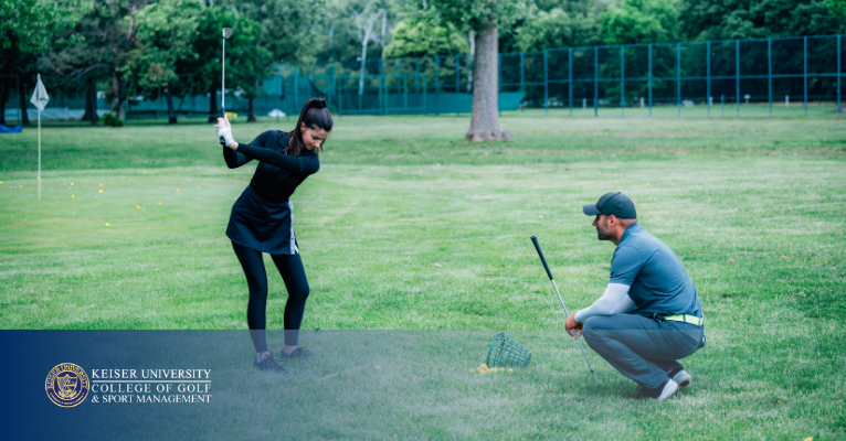 Golf coach observing a female student mid-swing on a practice field.