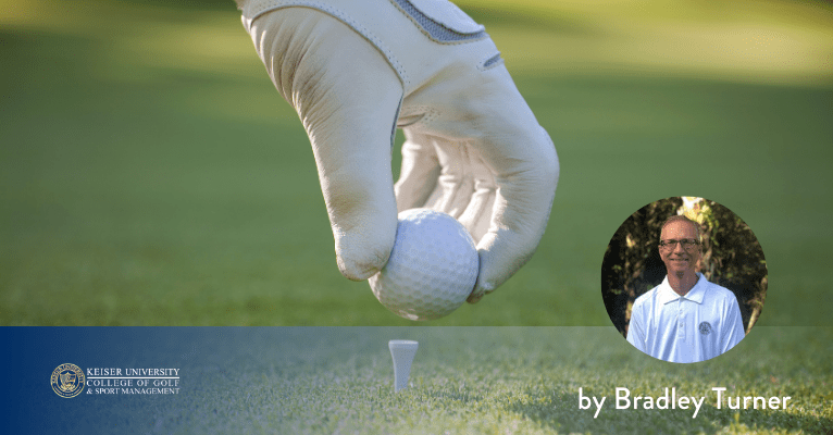 Golfer’s gloved hand setting a ball on a tee, ready for the opening shot on a neatly trimmed fairway.