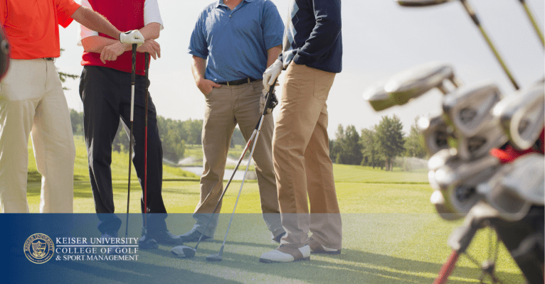 Group of golfers standing and talking on course with golf clubs, branded with Keiser University College of Golf logo.