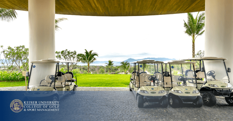 Golf carts parked under canopy with palm trees and mountains in background, branded with Keiser University College of Golf logo.