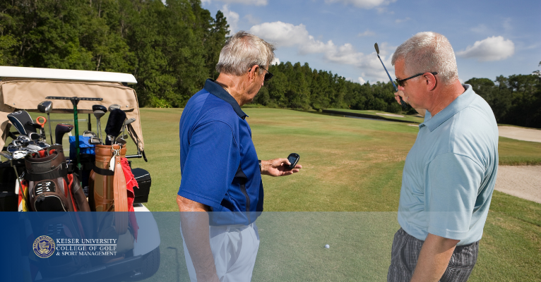 Two golfers checking a GPS device beside a golf cart on a sunny fairway.
